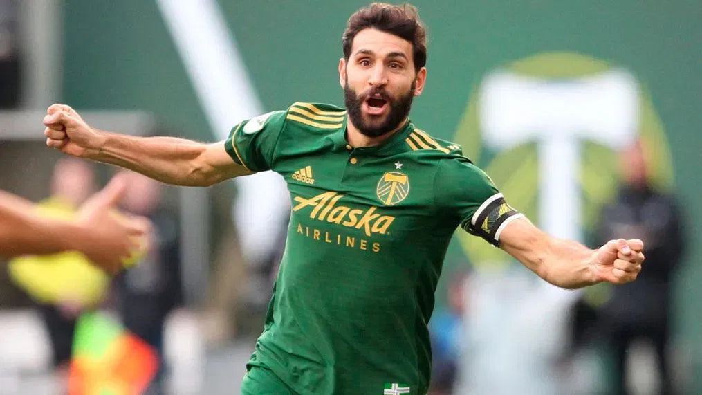Person in a green sports jersey celebrating with arms outstretched, featuring 'Portland Timbers'.
