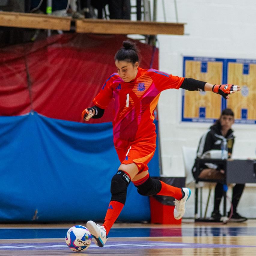 Person in red soccer uniform kicking a futsal ball on a court with a blue and red background