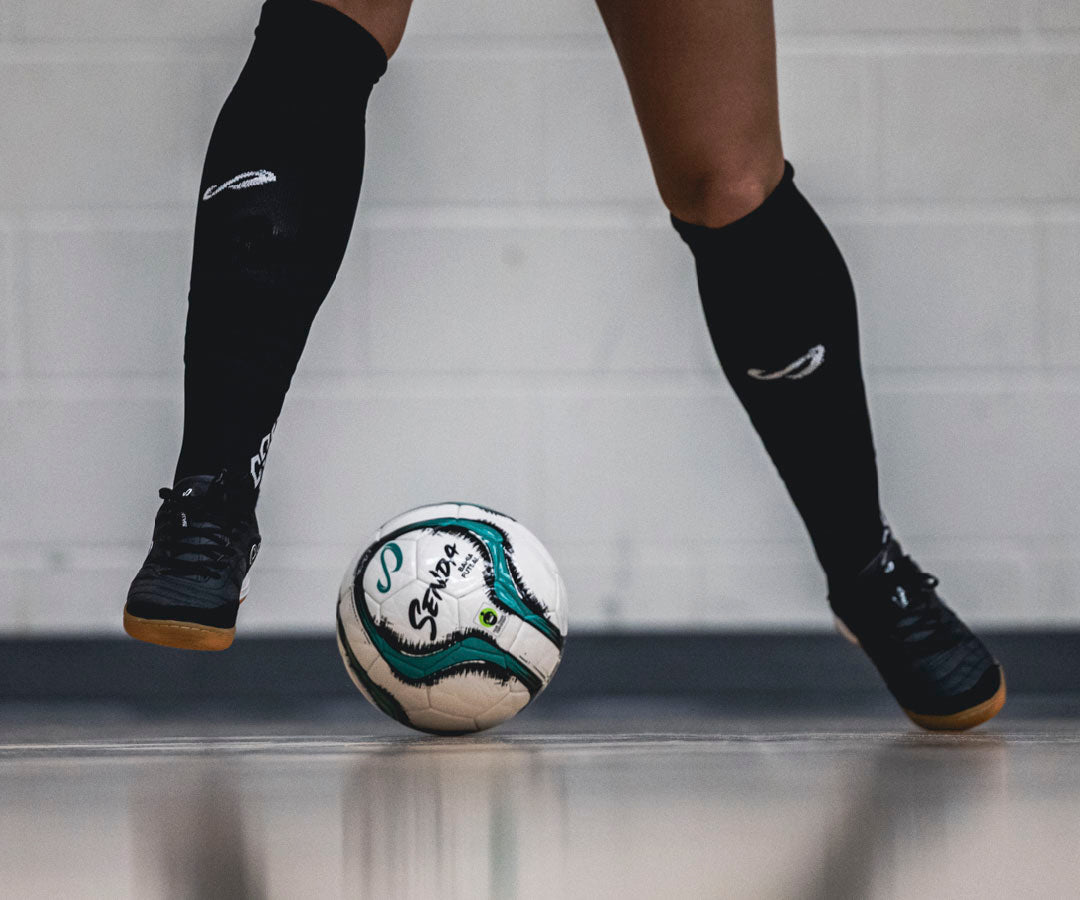 Person wearing futsal shoes and socks with a professional futsal ball on a neutral background