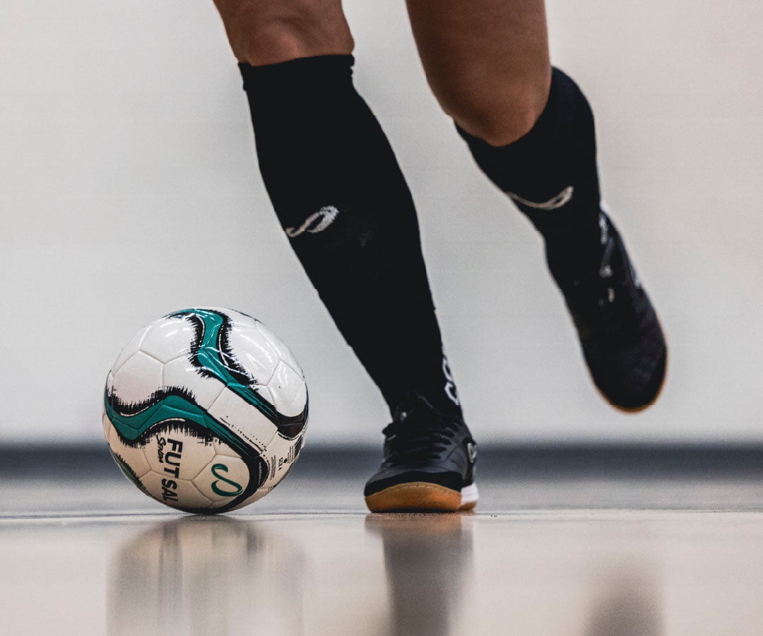 Person preparing to kick a professional futsal ball with black shoes and socks on a neutral background