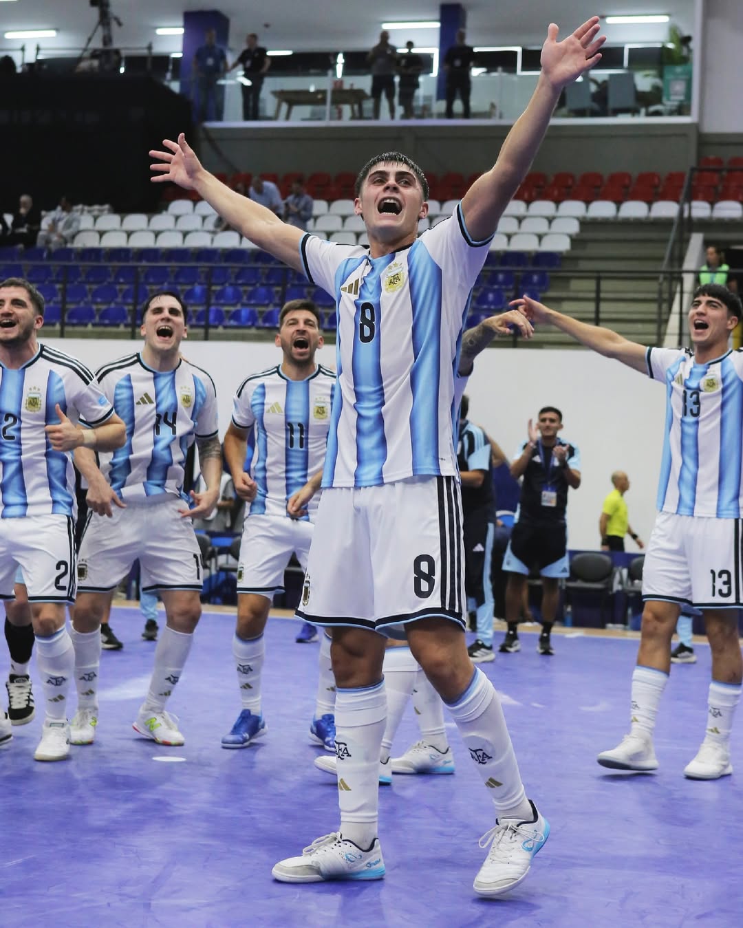 rgentine futsal players celebrating on a court with stadium seats in the background. Lucas Granda wearing Senda Ushuaia footwear.