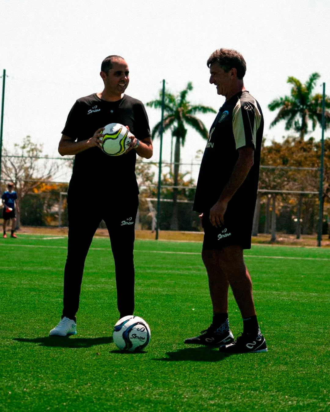 Mario Kempes and Santiago Halty, CEO & Founder of Senda,  on a soccer field with soccer balls, one holding a ball with a pattern.