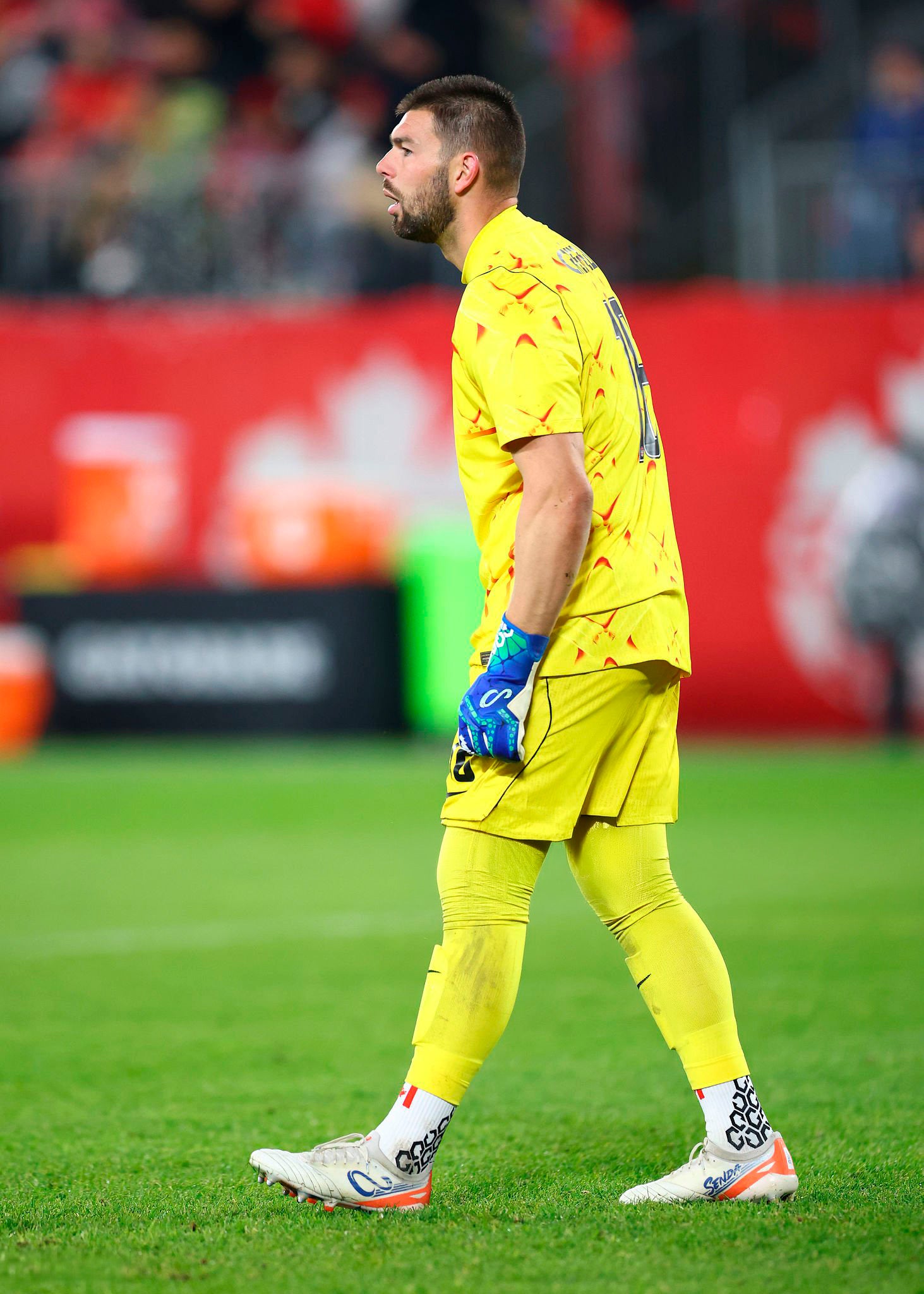 Goalkeeper Max Crepeau in yellow uniform walking on a soccer field with blurred spectators in the background
