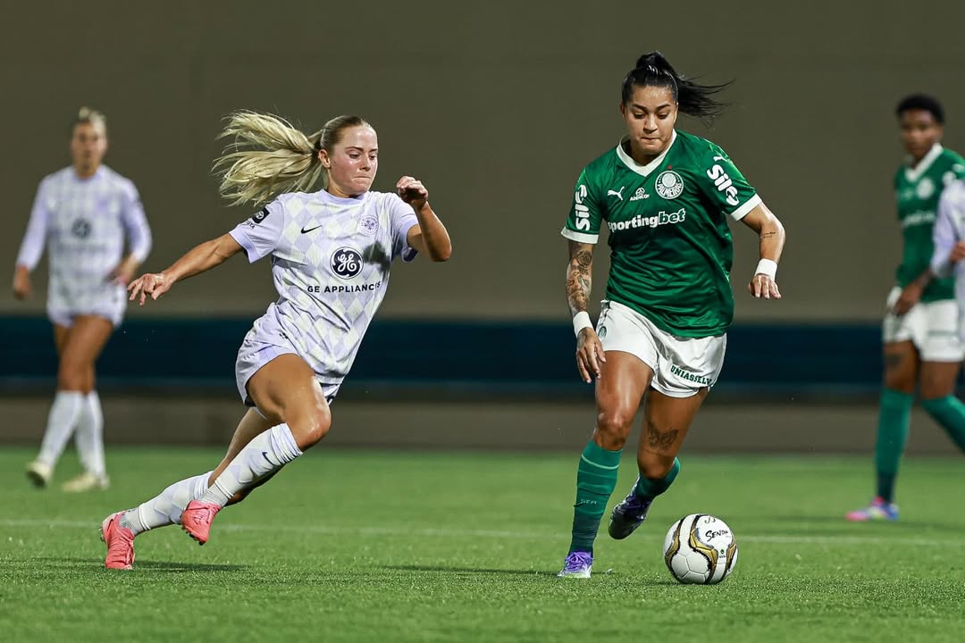 Two female soccer players in action on a field, one in a white uniform and the other in a green uniform.