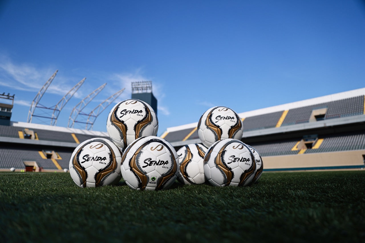 Soccer balls with 'Striker' branding on a grass field with stadium in the background