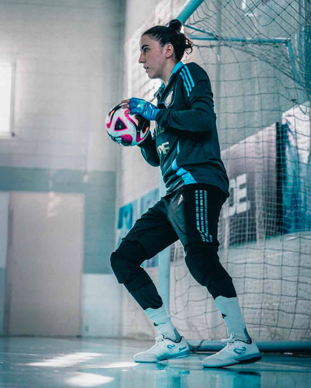 Person in sports gear holding a colorful ball in an indoor futsal facility.