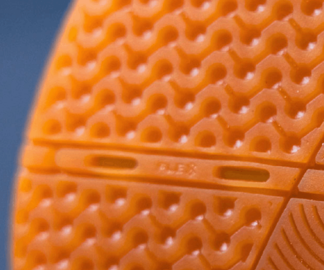 Close-up of an orange textured futsal sole with 'Flex' branding on a blue background.