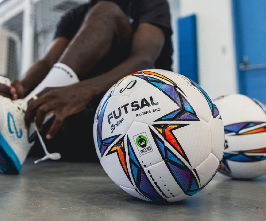 Eco Futsal ball with colorful design on a concrete floor, person sitting in the background.