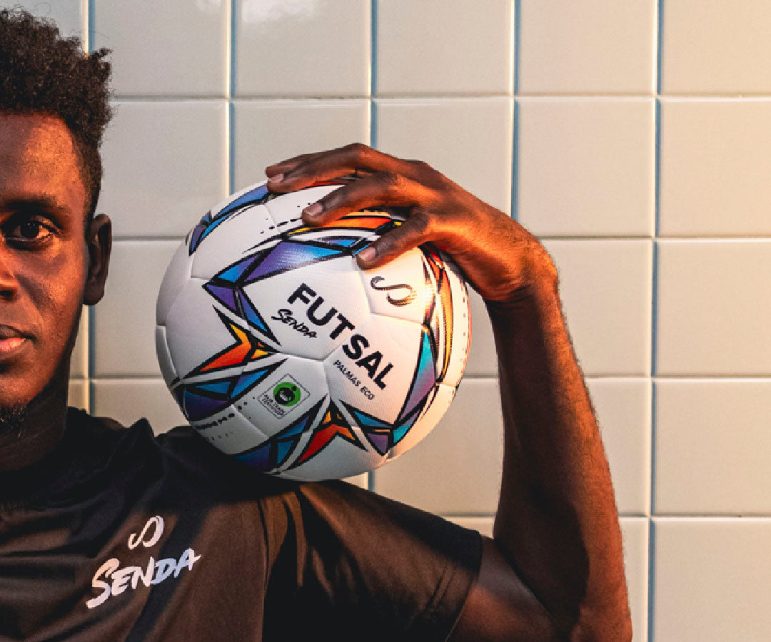 Person holding a colorful eco futsal ball against a tiled wall