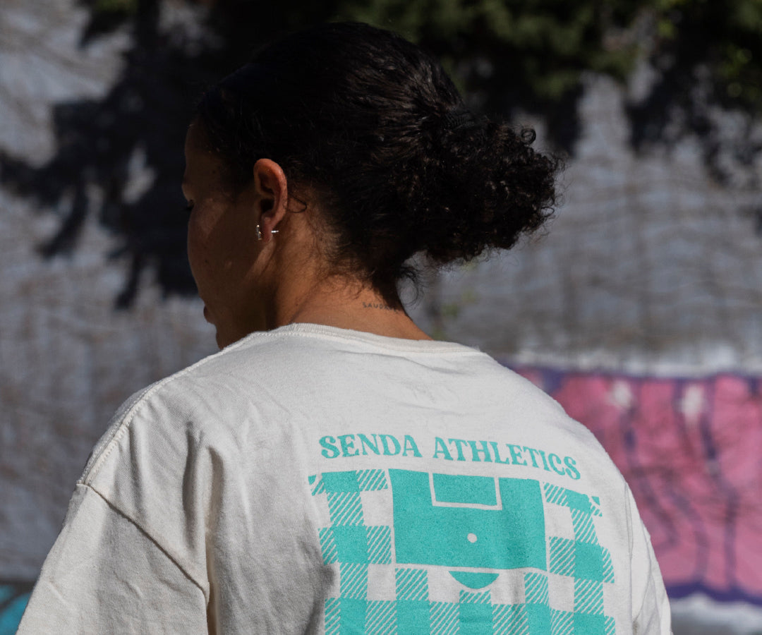Person wearing a 'Senda Athletics' shirt with a checkered design, standing outdoors.