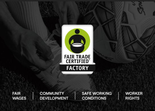 A Fair Trade Certified Factory badge centered over a dark, moody soccer-themed background showing hands tying a Senda shoe and a soccer ball. Text at the bottom reads: FAIR WAGES | COMMUNITY DEVELOPMENT | SAFE WORKING CONDITIONS | WORKER RIGHTS.