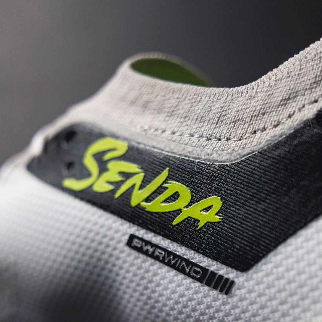 Close-up of a gray shoe with a green 'Senda' logo on a dark background.Turf Shoes.