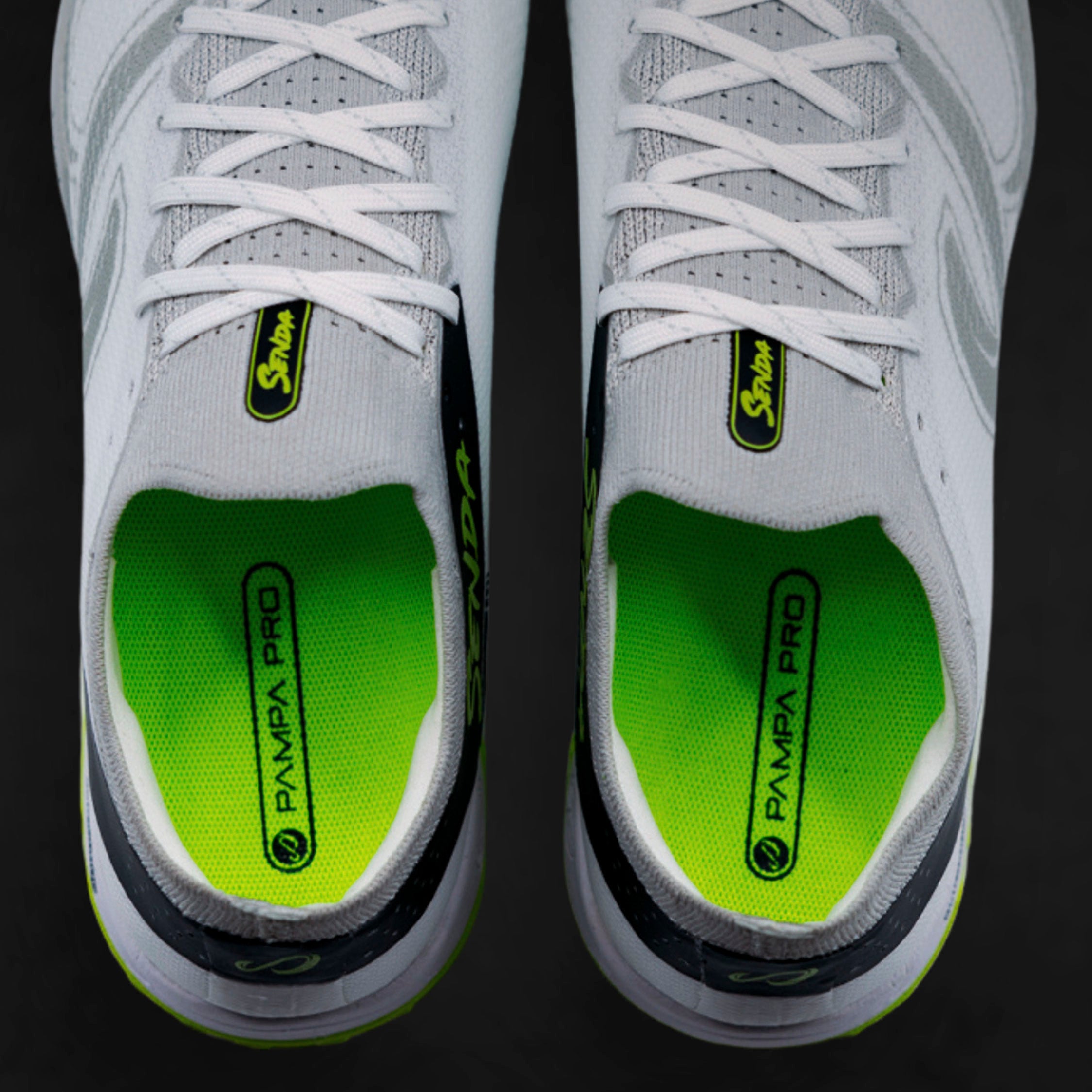 Gray sneakers with white laces and green soles on a black background. Turf Shoes.