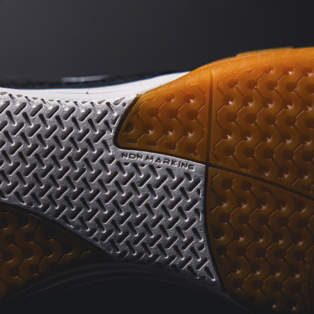 Close-up of a futsal shoe sole with orange and gray pattern on a black background