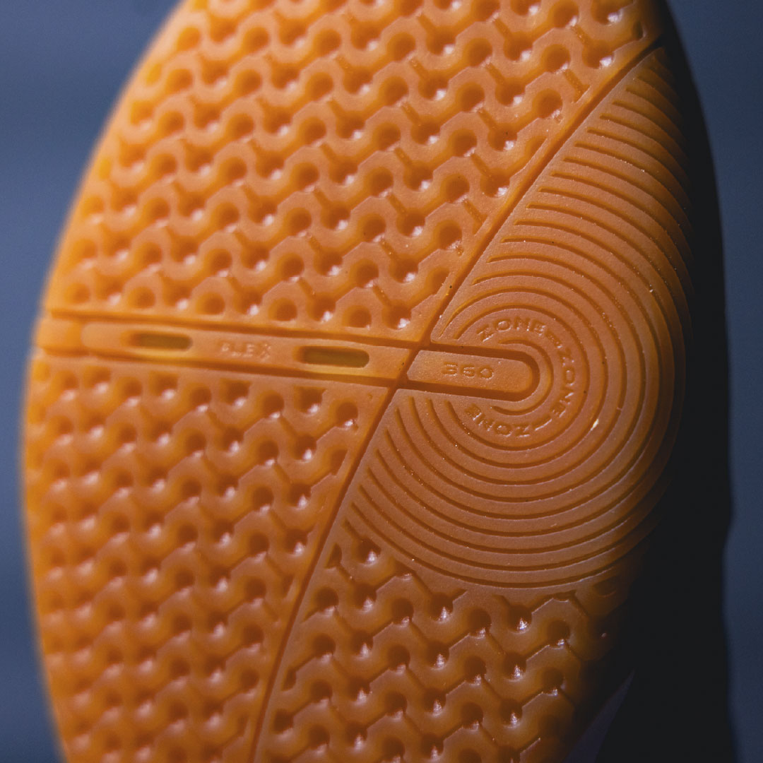 Close-up of a textured  orange futsal sole with brand logo on a dark background