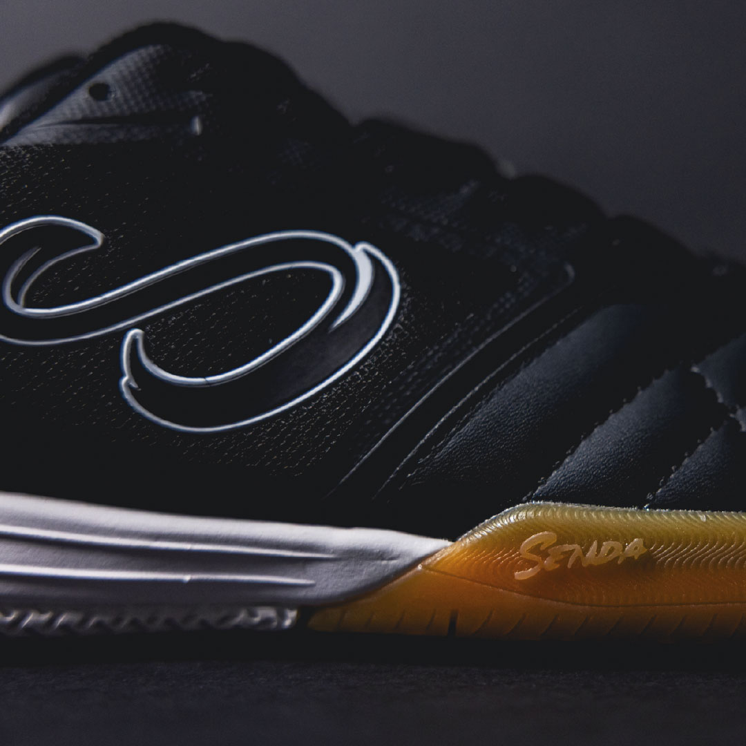 Close-up of a black futsal shoe with a yellow sole on a dark background