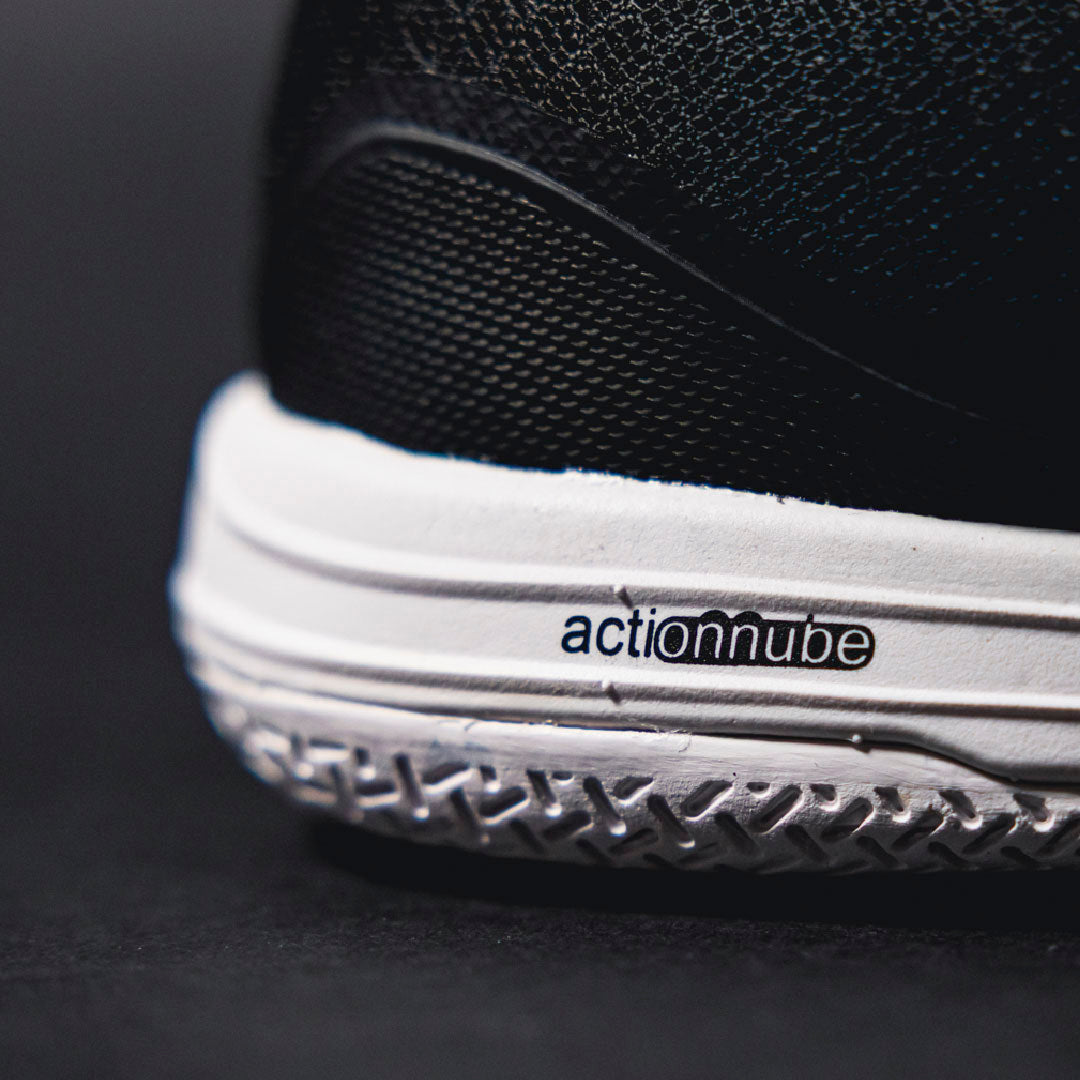 Close-up of a black and white futsal shoe with 'actionnube' branding on a dark background