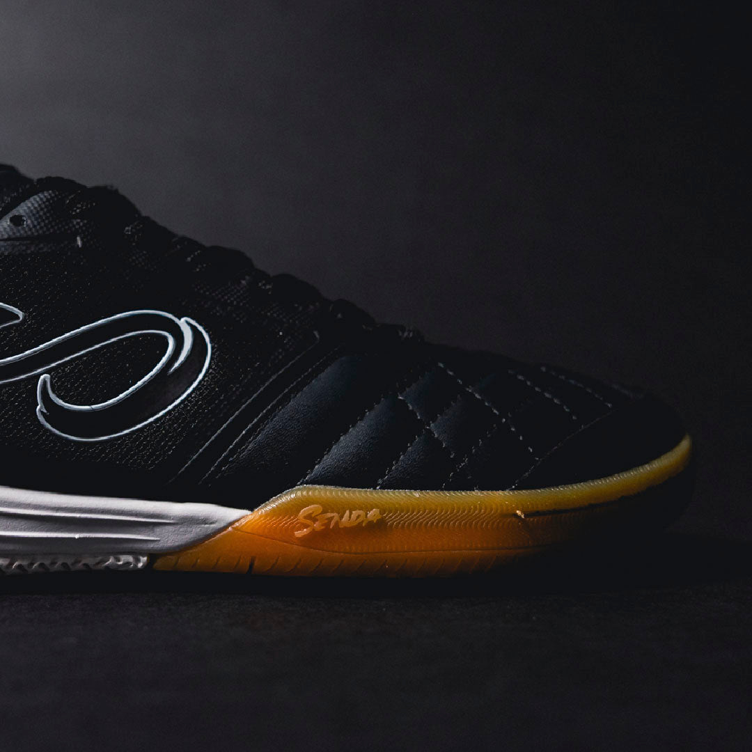 Black sports futsal shoe with yellow sole on a dark background