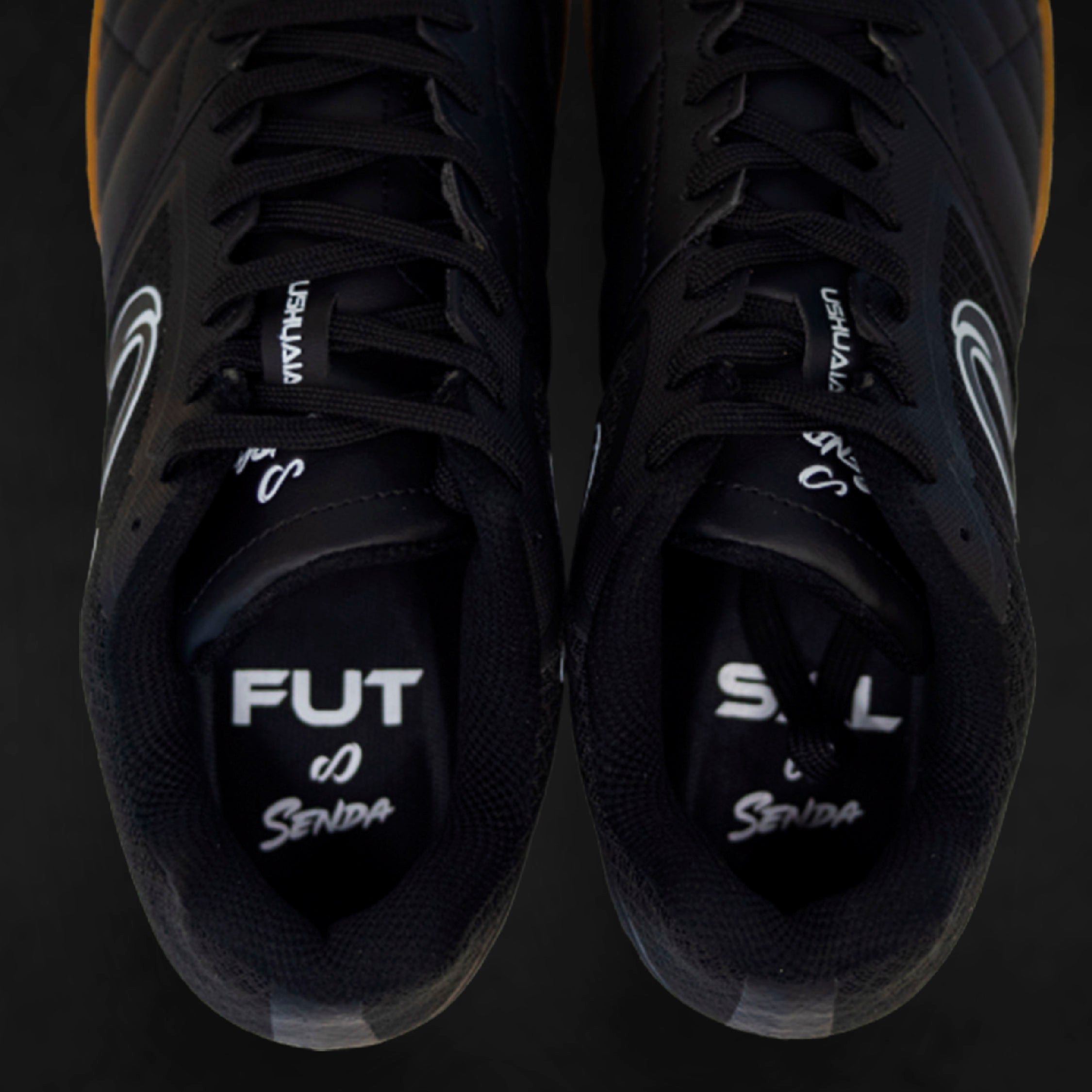 Black athletic futsal shoes with visible branding on a dark background.